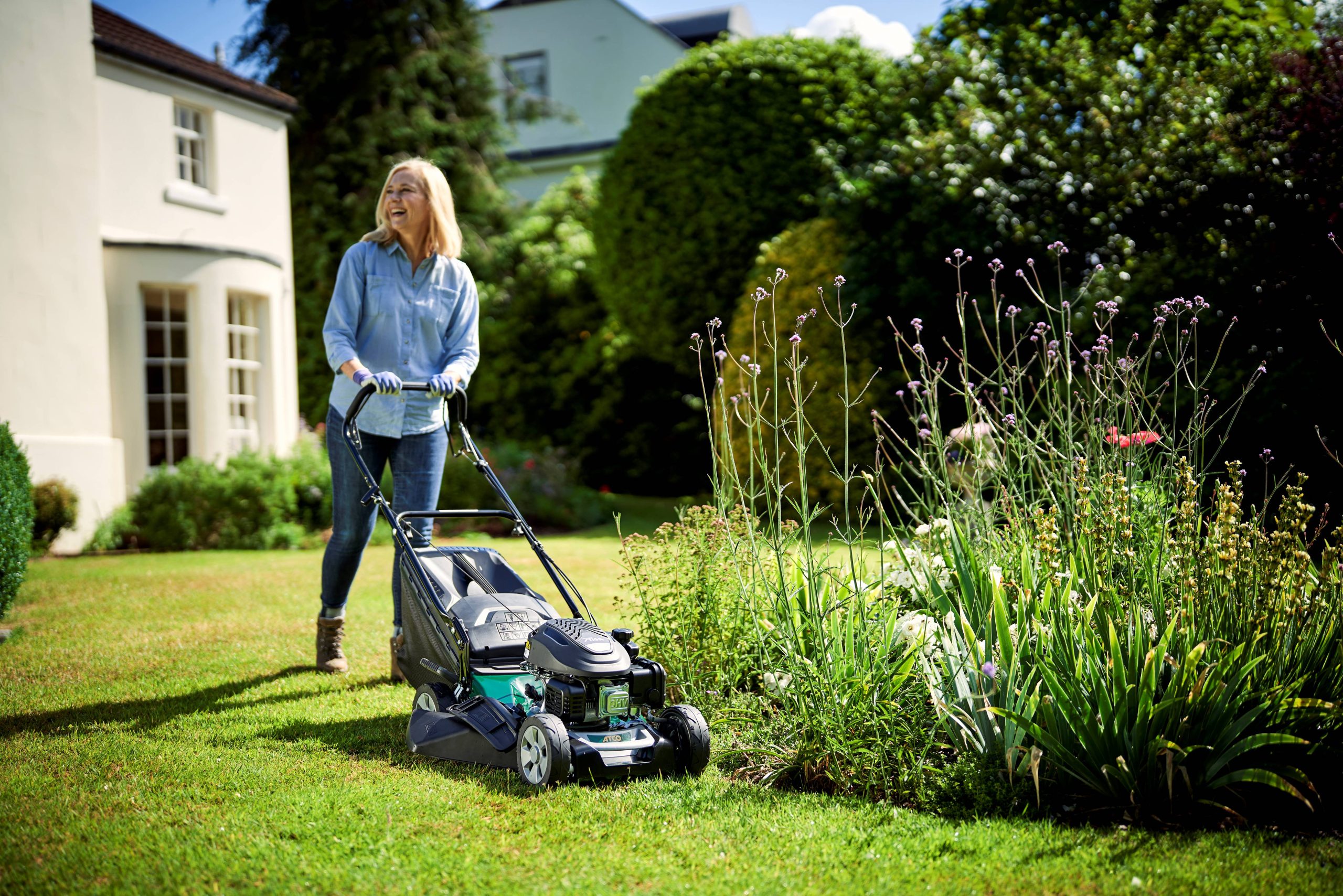 woman mowing lawn with green lawnmower